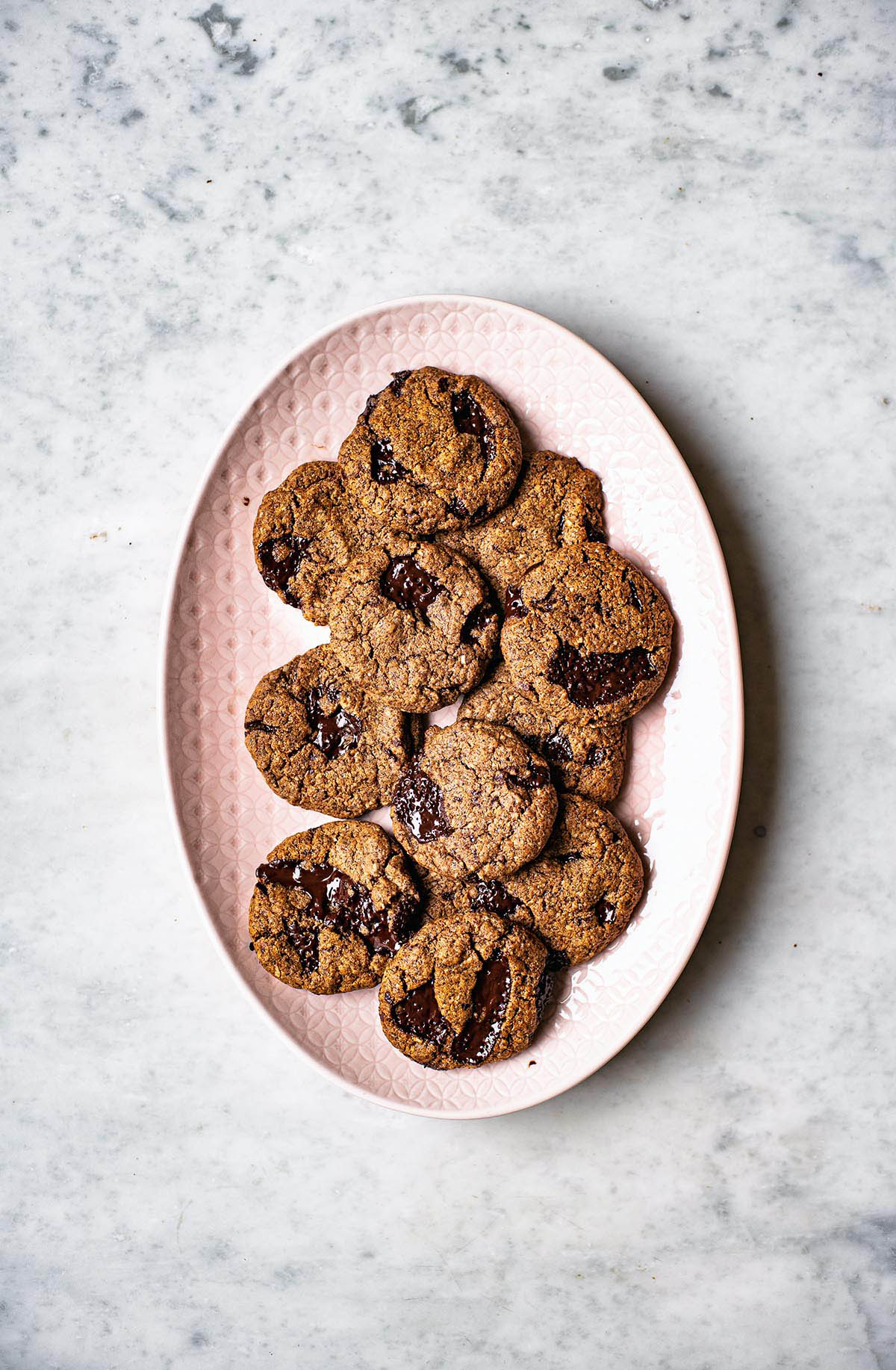 Several chocolate chunk cookies on a large pink serving platter.