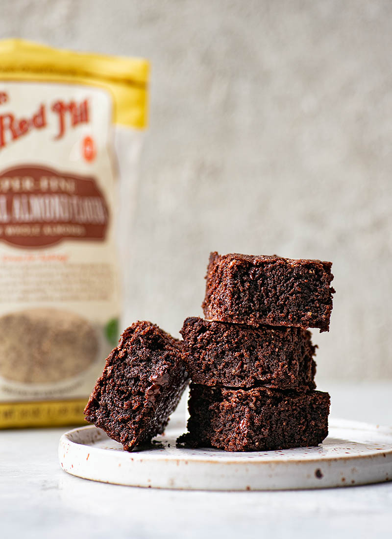 Stack of three brownies with one leaning against the stack, with a bag of almond flour in the background.