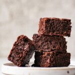 Stack of three brownies on a speckled plate with another brownie leaning against the stack.