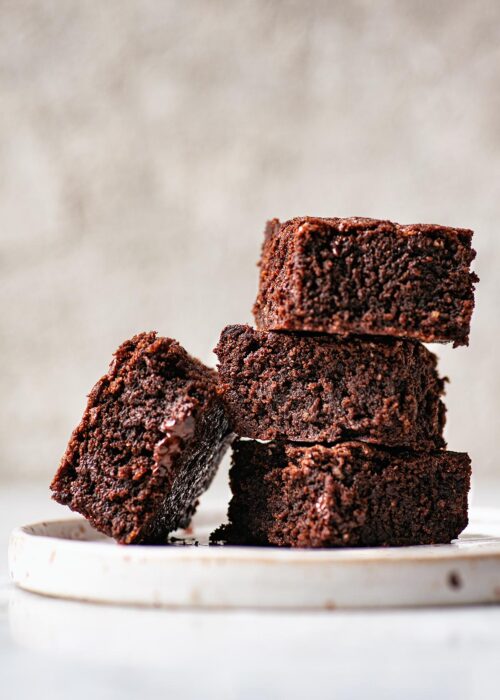 Stack of three brownies on a speckled plate with another brownie leaning against the stack.