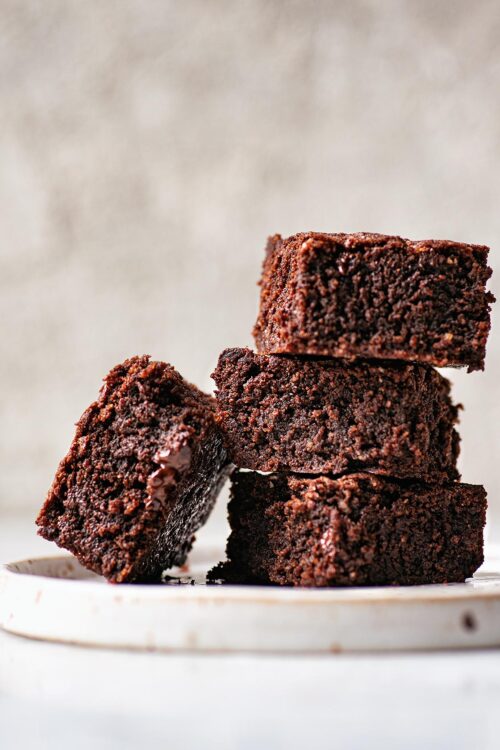 Stack of three brownies on a speckled plate with another brownie leaning against the stack.
