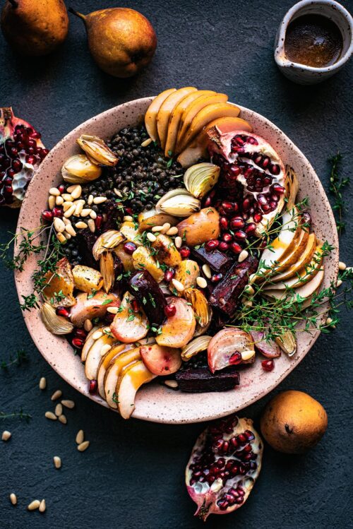 Lentil salad with beets, shallots, pomegranate, and pears in a large pink bowl.