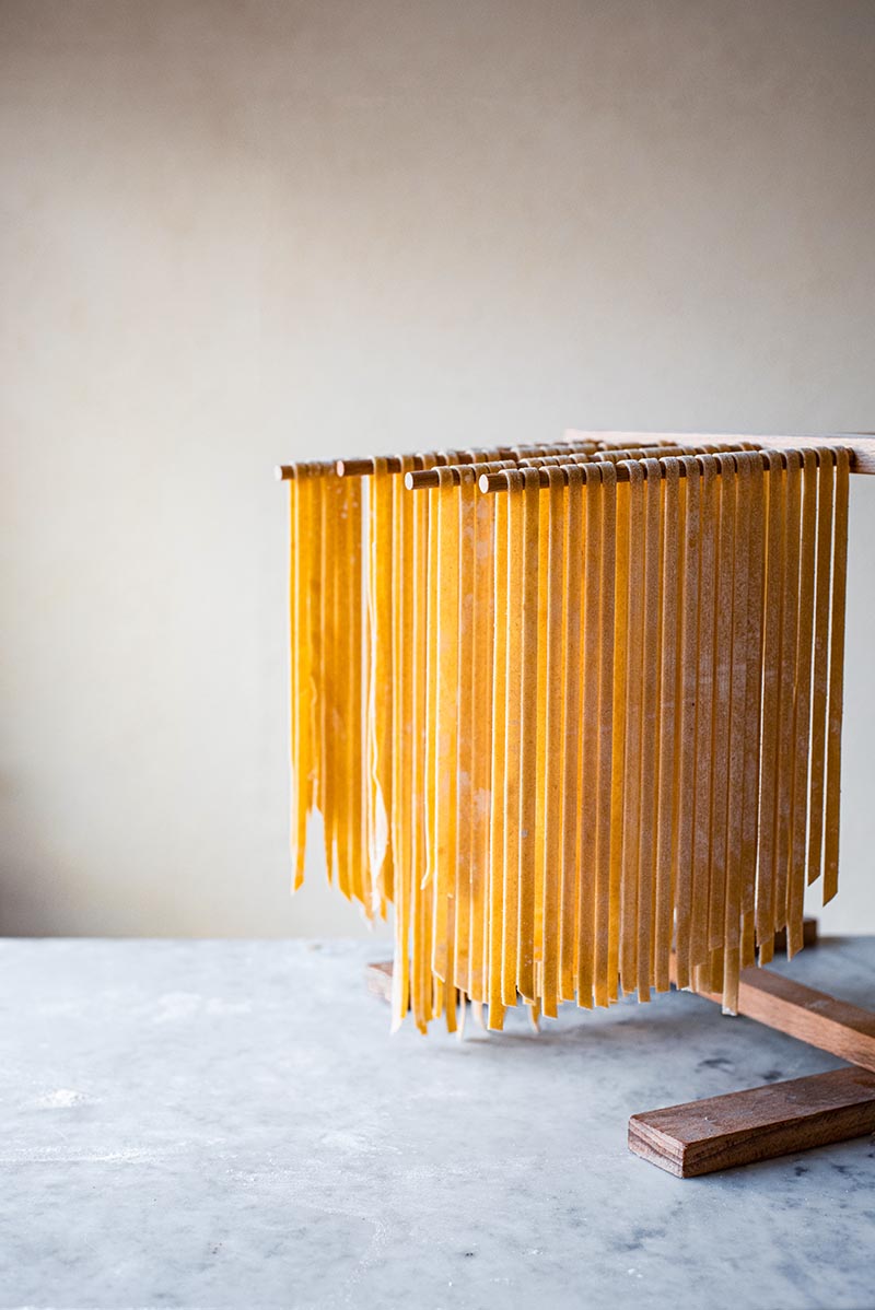 Kamut pasta cut into tagliatelle drying on a wooden wrack.