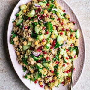 Top view of quinoa salad with chickpeas, vegetables, and pomegranate on a pink platter.