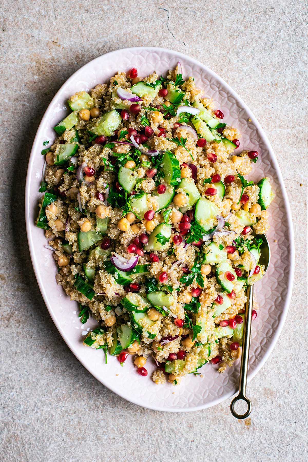 Top view of quinoa salad with chickpeas, vegetables, and pomegranate on a pink platter.