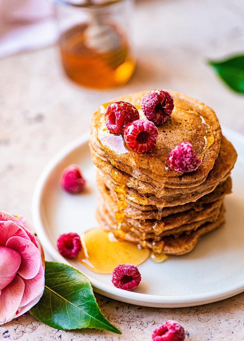 Stack of American style pancakes topped with frozen raspberries and syrup.