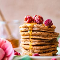 Stack of American style pancakes topped with frozen raspberries and syrup.