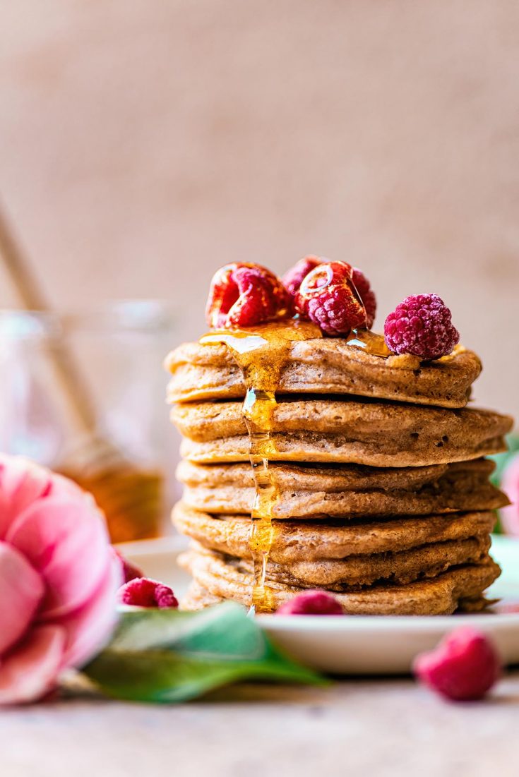 Stack of American style pancakes topped with frozen raspberries and syrup.