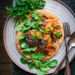 A large plate with naan, tomato sauce, black bean meatballs, and greens.