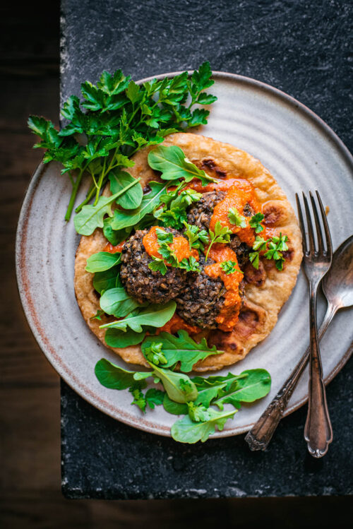 A large plate with naan, tomato sauce, black bean meatballs, and greens.
