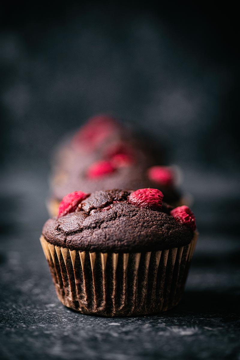 Chocolate muffins topped with raspberries in a row.