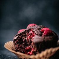 Chocolate raspberry muffin, close up in a paper liner, with a bite taken out to show interior texture.