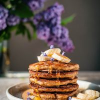 Stack of pancakes topped with bananas and lilac blossoms.