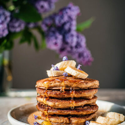 Stack of pancakes topped with bananas and lilac blossoms.