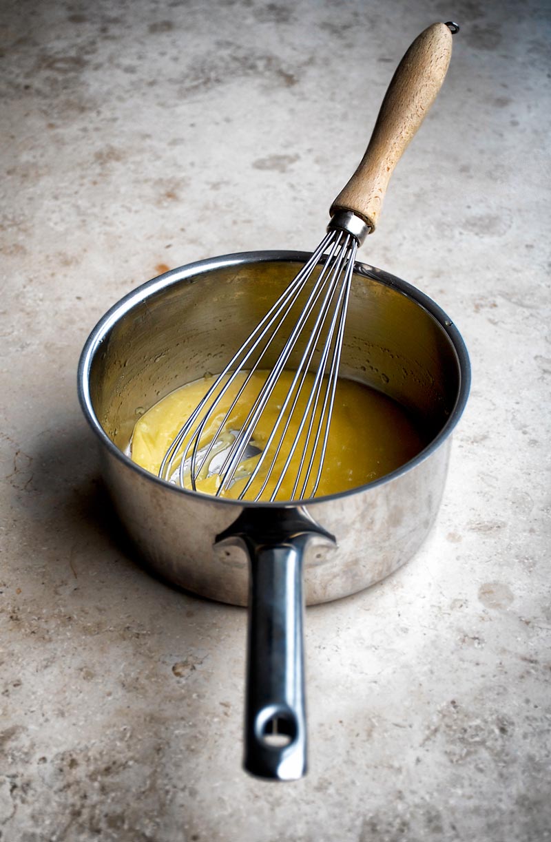 Small saucepan with mix of cacao butter and honey with whisk.