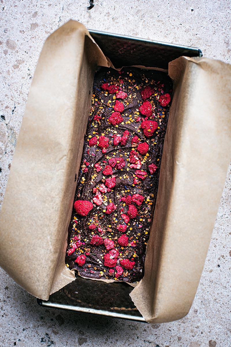 Raw chocolate topped with dried raspberries and bee pollen in a parchment lined bread tin.