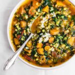 A bowl of soup with carrots, spinach, and lentils with rice.