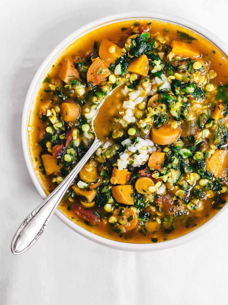 A bowl of soup with carrots, spinach, and lentils with rice.