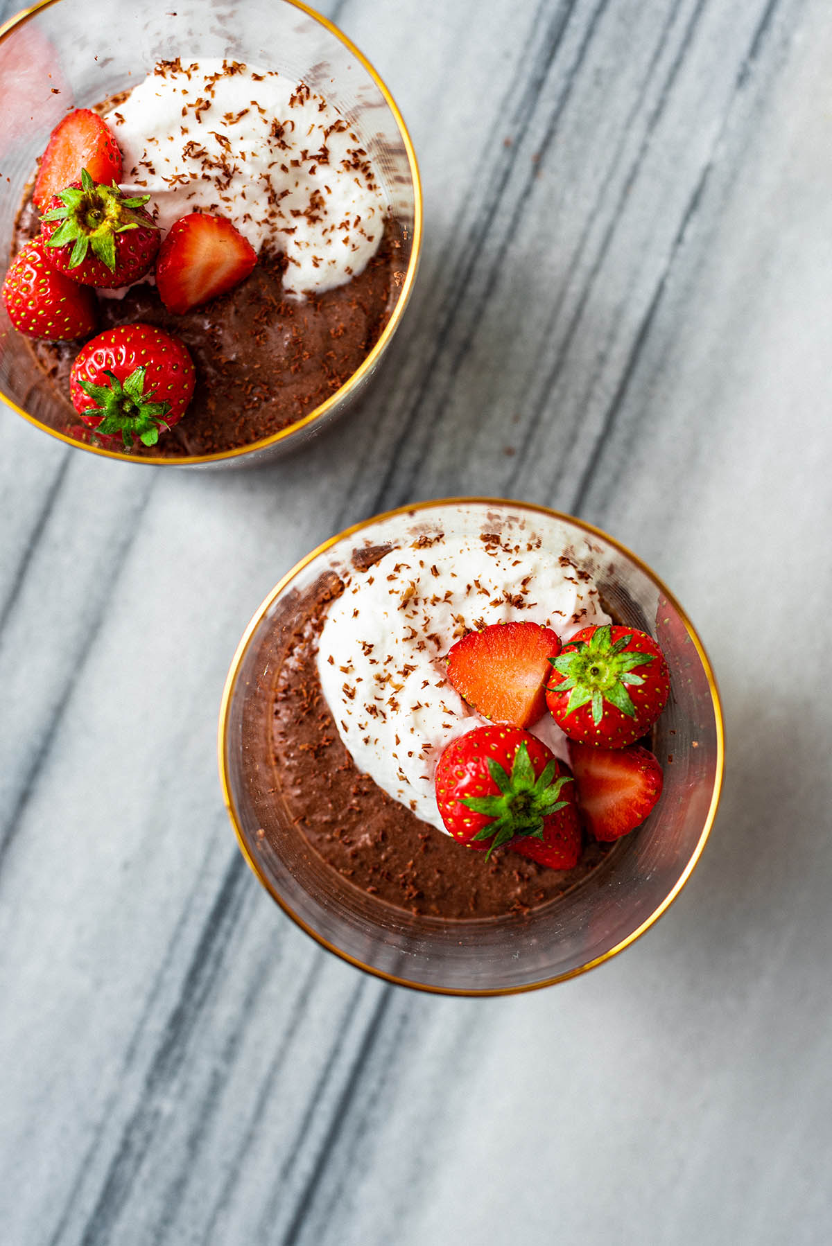 Chocolate chia mousse in two a glasses with whipped cream and strawberries.