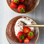 Close up of two cups of chocolate mousse with whipped cream and strawberries.