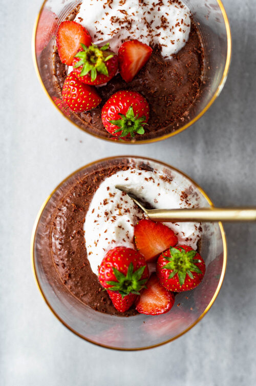 Close up of two cups of chocolate mousse with whipped cream and strawberries.