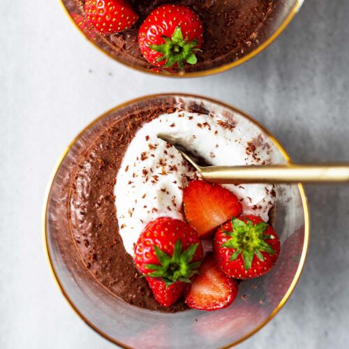 Close up of two cups of chocolate mousse with whipped cream and strawberries.