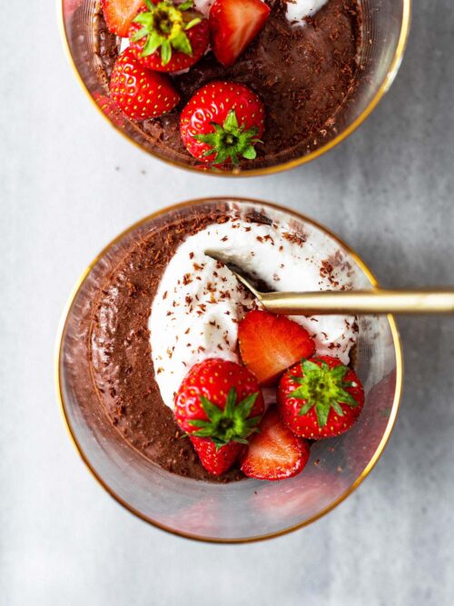 Close up of two cups of chocolate mousse with whipped cream and strawberries.