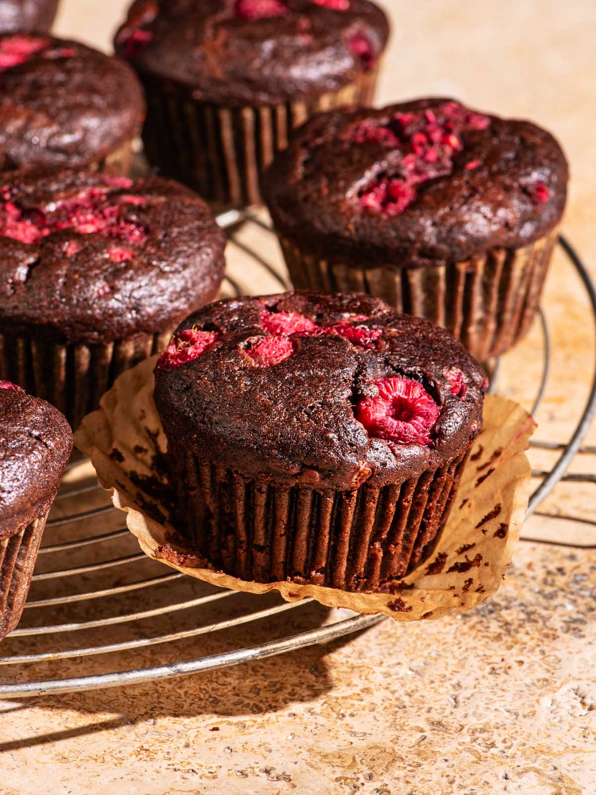 Several chocolate muffins with raspberries on a wire rack.