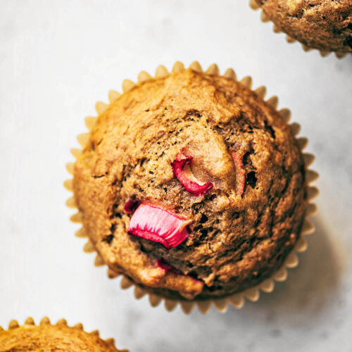 Three rhubarb muffins in a diagonal row, top down view.