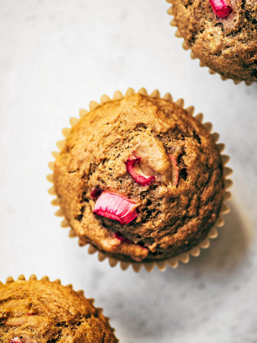 Three rhubarb muffins in a diagonal row, top down view.