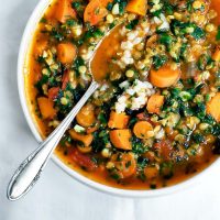 A bowl of carrot red lentil soup with spinach and rice, with a spoon.