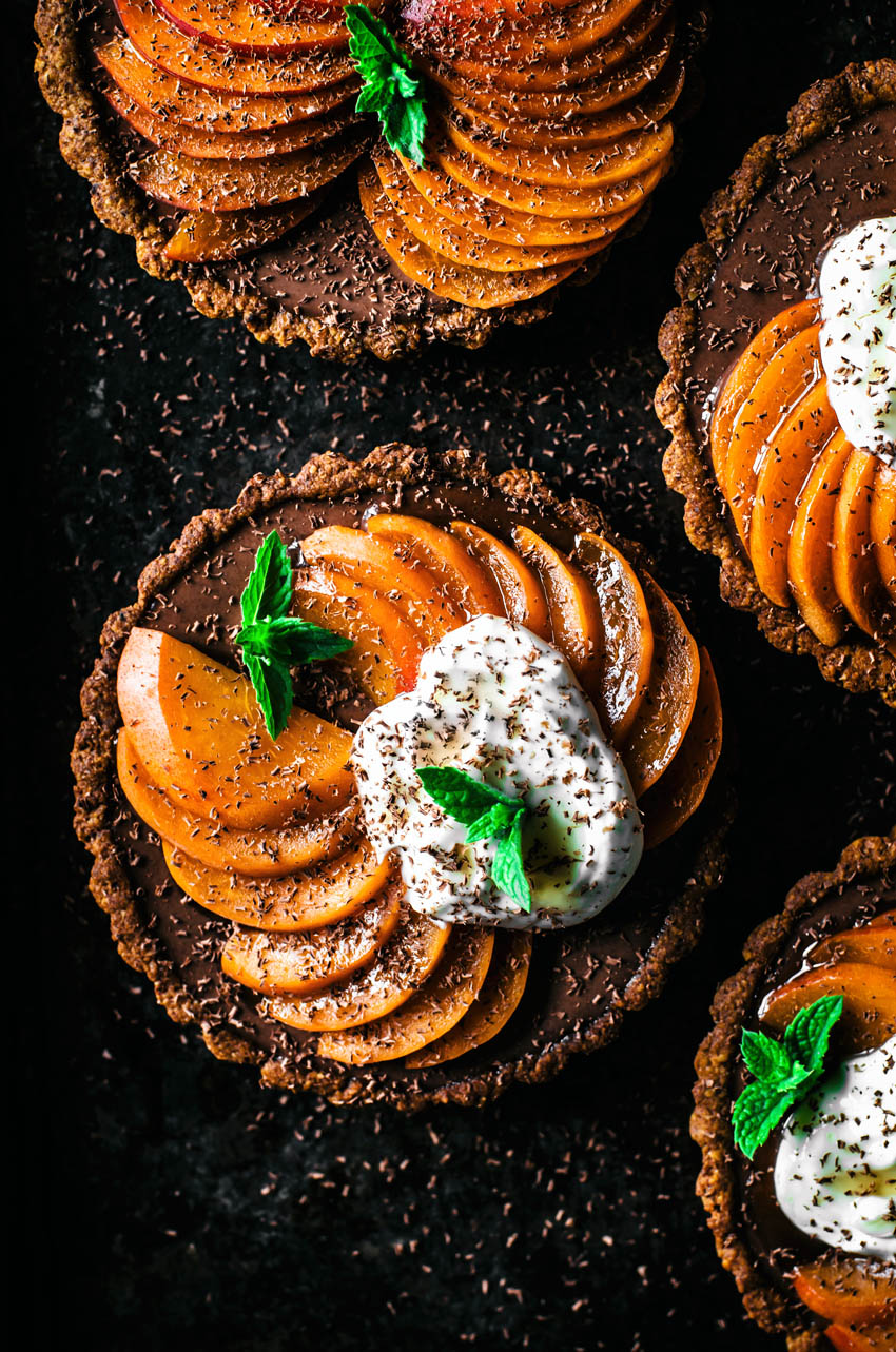 Top down view of four chocolate ganache filled tarts topped with sliced apricots and yogurt.