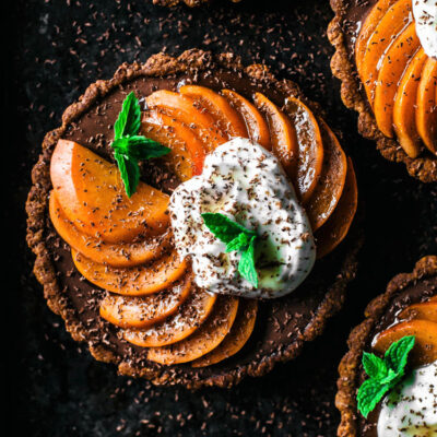 Top down view of four chocolate ganache filled tarts topped with sliced apricots and yogurt.