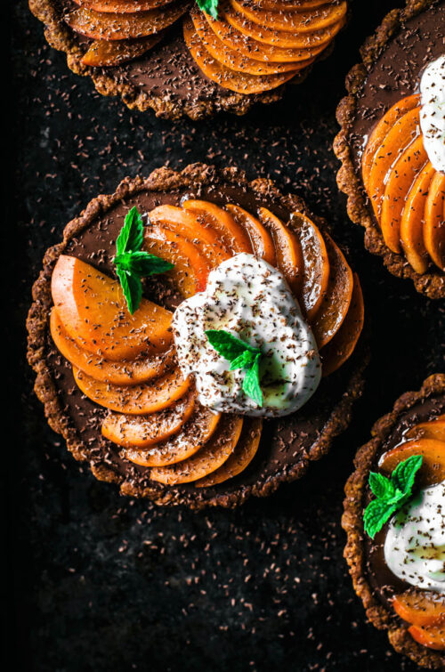 Top down view of four chocolate ganache filled tarts topped with sliced apricots and yogurt.