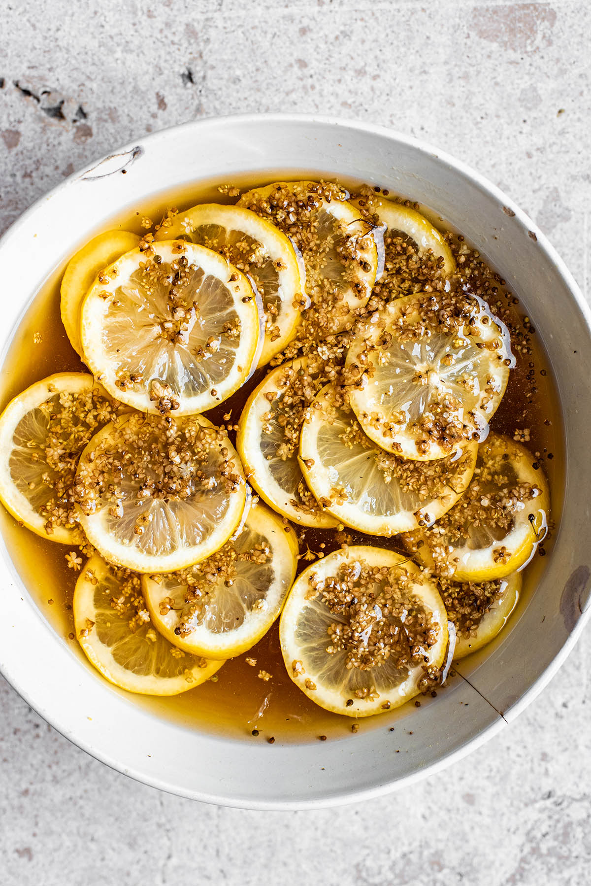 Lemon slices and elderflowers in a bowl floating in a dark syrup.