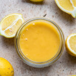 Lemon curd in a glass jar surrounded by lemons.