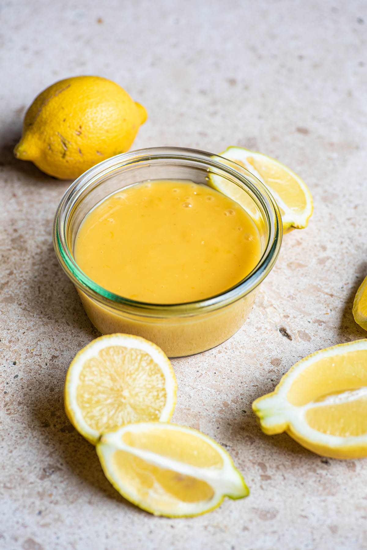 Lemon curd in a low glass jar surrounded by lemons.