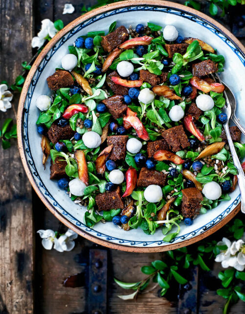 A big serving bowl with lamb's lettuce, blueberries, rhubarb, and croutons on a wooden crate.