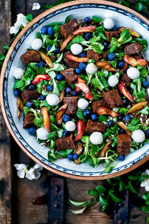 A big serving bowl with lamb's lettuce, blueberries, rhubarb, and croutons on a wooden crate.