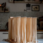 Long fettuccine noodles drying on a wooden pasta drying rack.