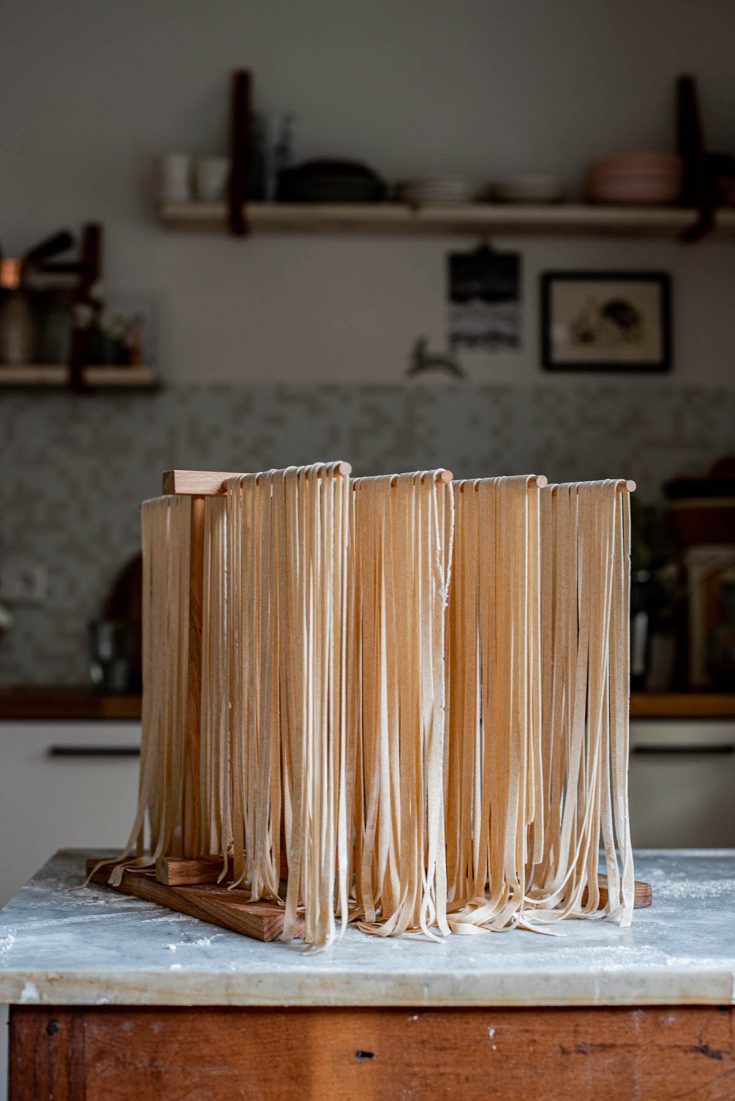 Long fettuccine noodles drying on a wooden pasta drying rack.