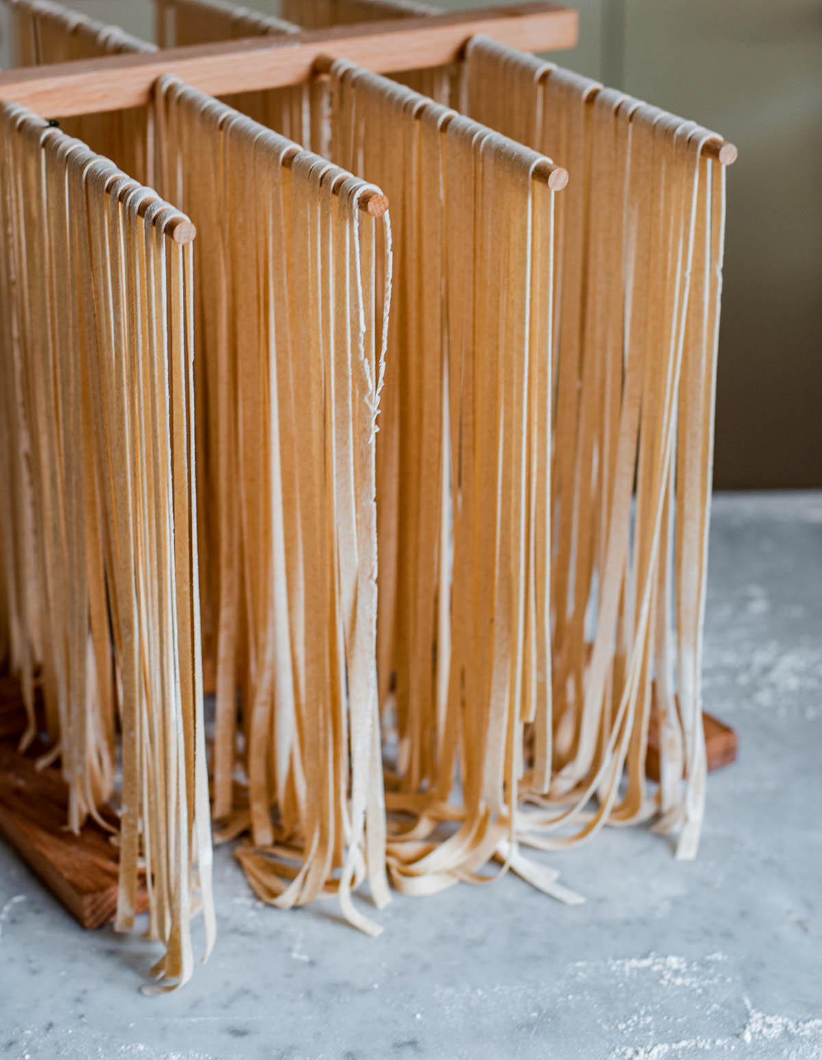 Spelt pasta cut into fettuccine drying on a wooden rack.