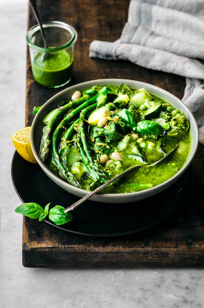 Asparagus white bean soup with pesto in a bowl with lemons on the side.
