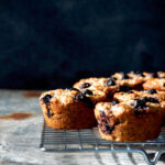 Blueberry muffins on a metal cooling rack in front of a dark background.