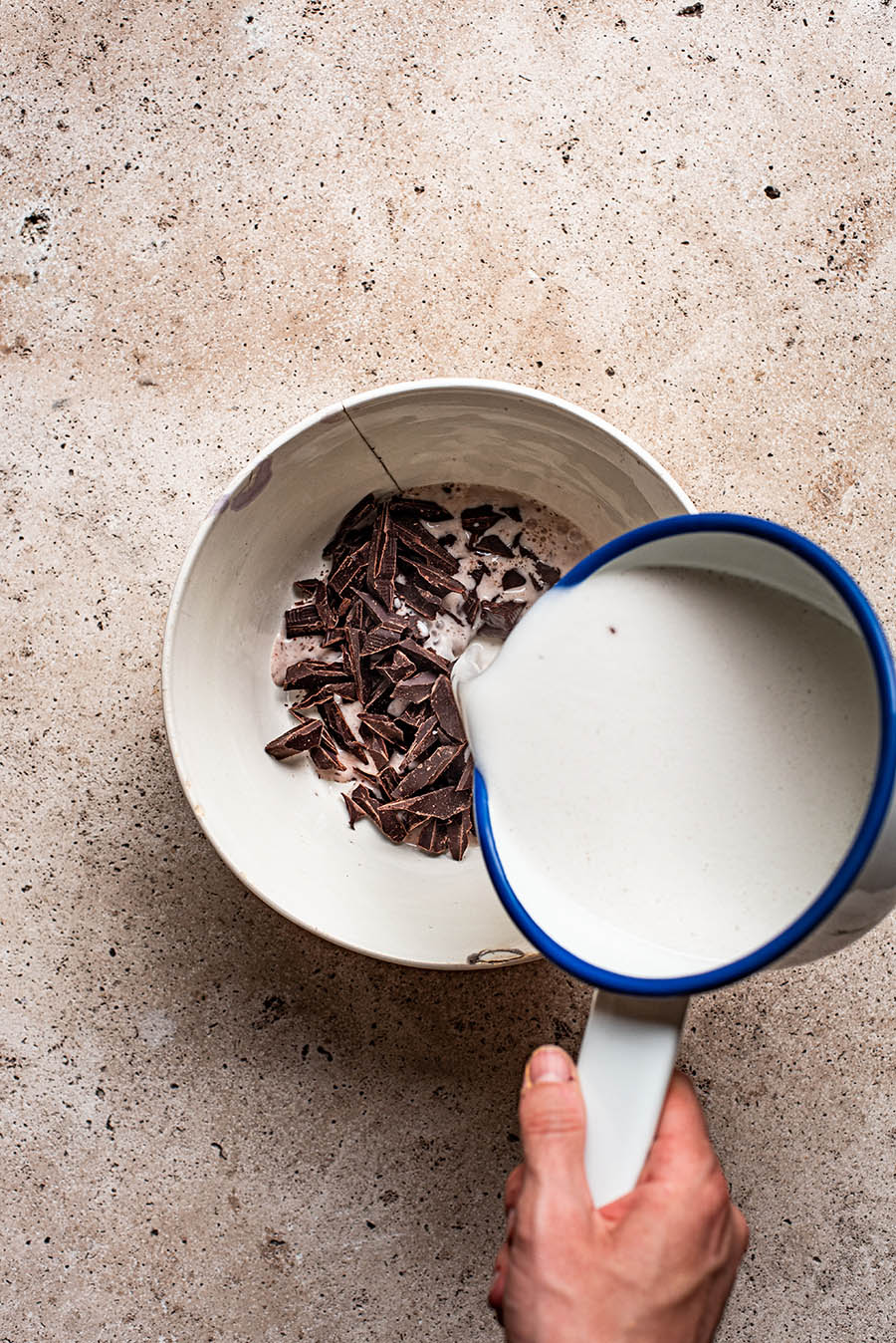Hot coconut milk being poured over chopped chocolate in a bowl.
