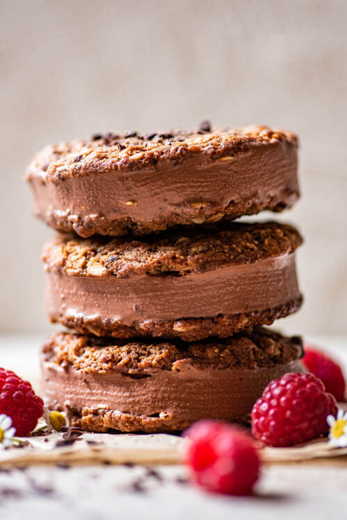 A stack of three oatmeal cookie chocolate ice cream sandwiches, decorated with raspberries and flowers.