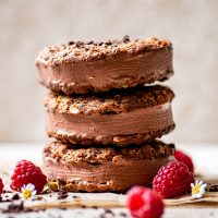 A stack of three oatmeal cookie chocolate ice cream sandwiches, decorated with raspberries and flowers.