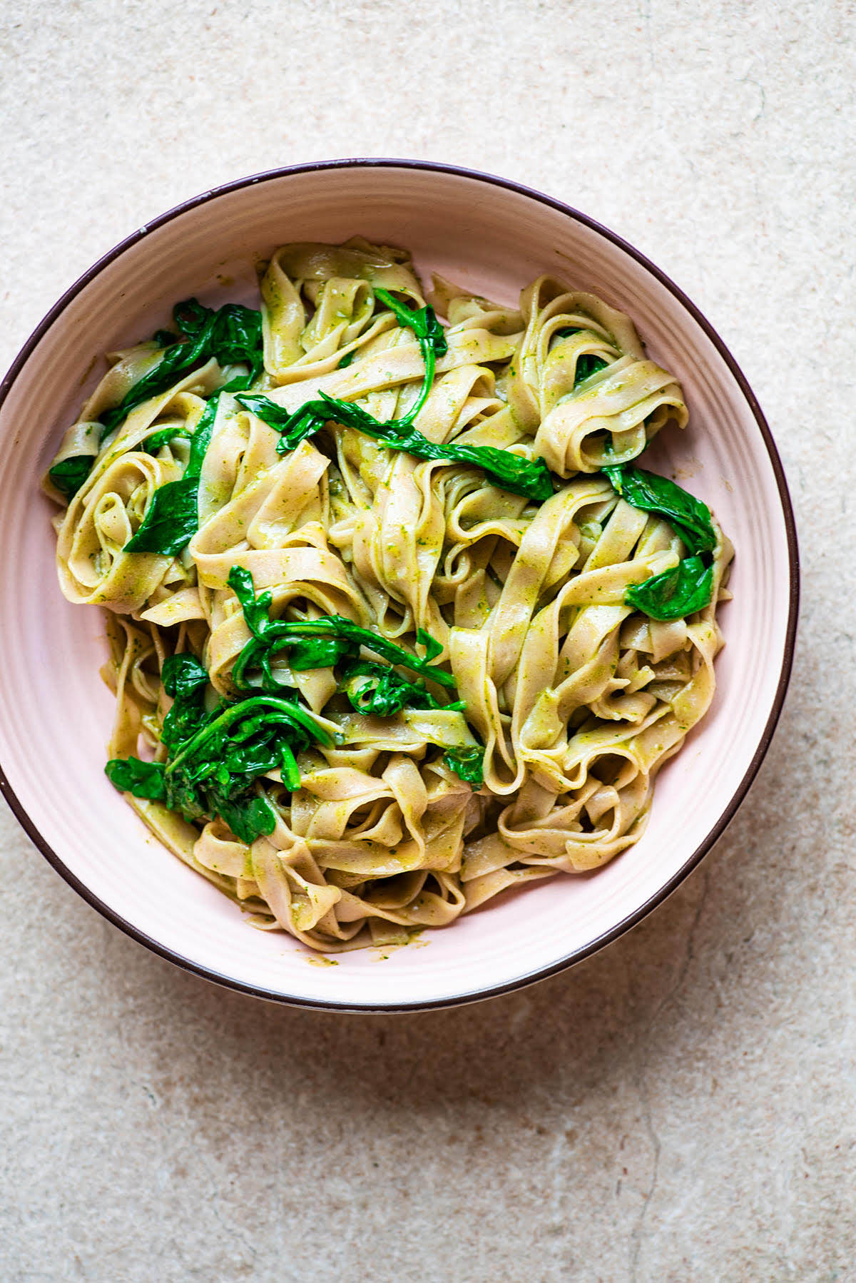 A bowl of fettuccine with pesto and greens.