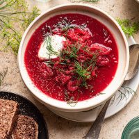 A bowl of red beet borscht topped with dill and yogurt.