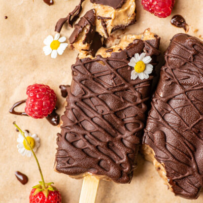 Dark chocolate coated popsicles on parchment paper with flowers and berries, one cut to show interior.